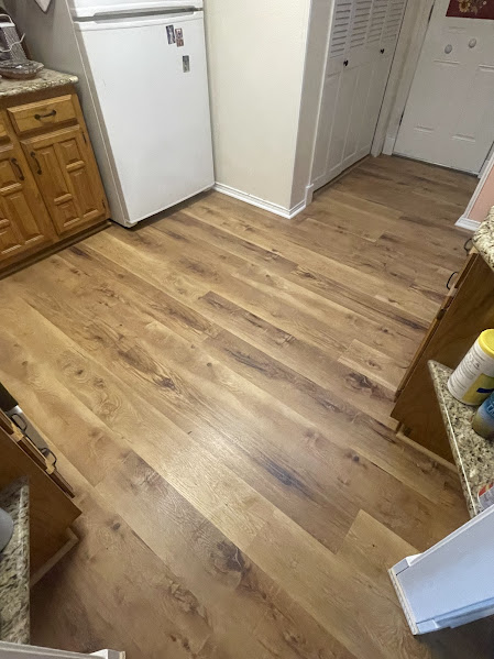 Wooden kitchen floor with light brown planks and white appliances in the background.